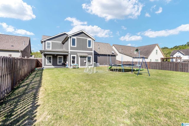 back of property with board and batten siding, a fenced backyard, a trampoline, and a lawn