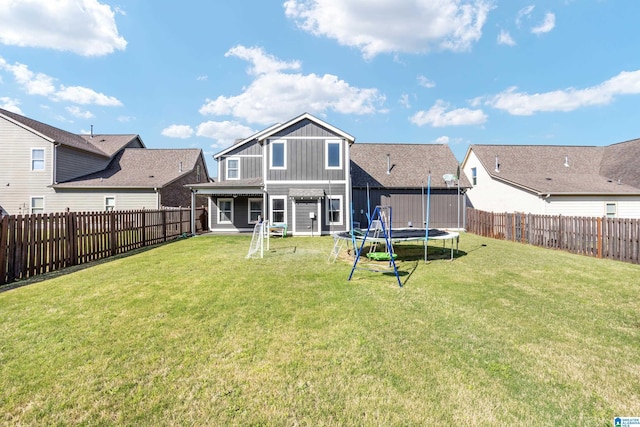 back of property featuring a trampoline, a yard, a fenced backyard, and board and batten siding