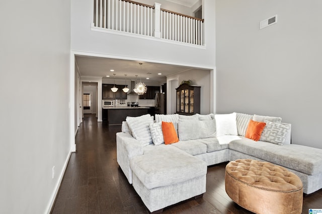 living room featuring a towering ceiling, visible vents, ornamental molding, and dark wood-style floors