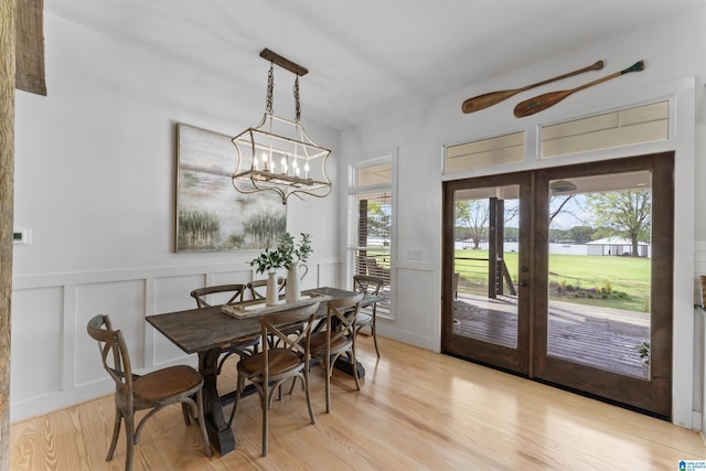 dining area featuring french doors, a decorative wall, a wainscoted wall, and light wood-type flooring