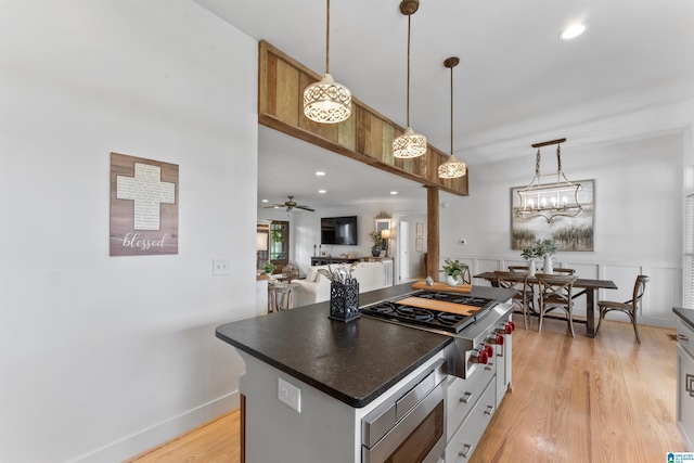 kitchen with hanging light fixtures, a kitchen island, dark countertops, light wood finished floors, and appliances with stainless steel finishes