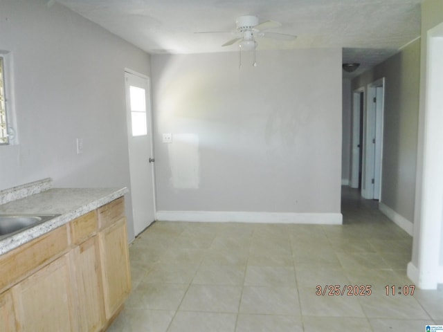 kitchen featuring light countertops, light tile patterned floors, baseboards, a ceiling fan, and light brown cabinets