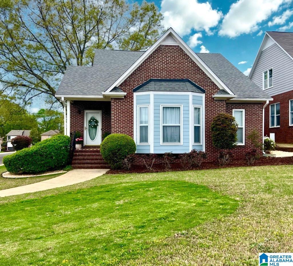 view of front of home with a front yard, brick siding, and roof with shingles