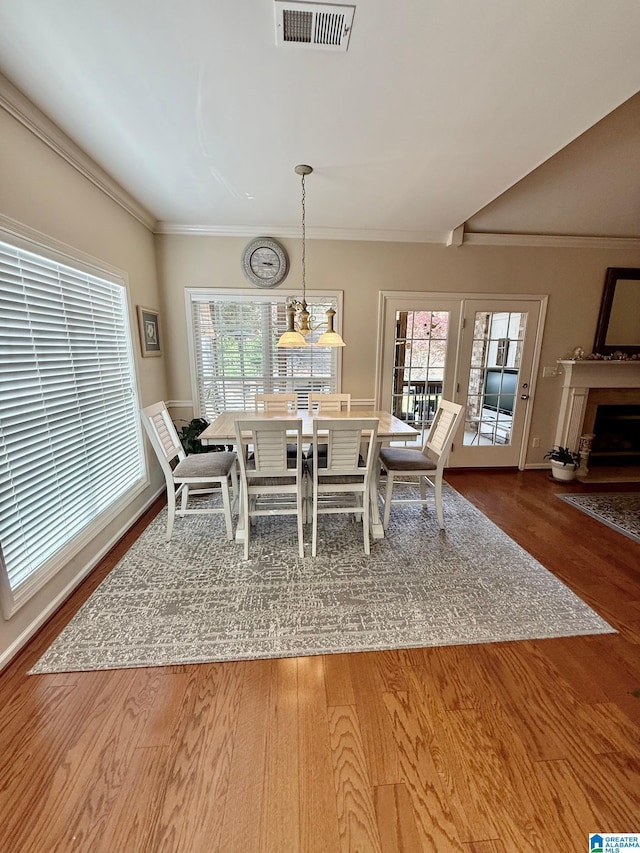 dining room with a fireplace with flush hearth, ornamental molding, visible vents, and wood finished floors