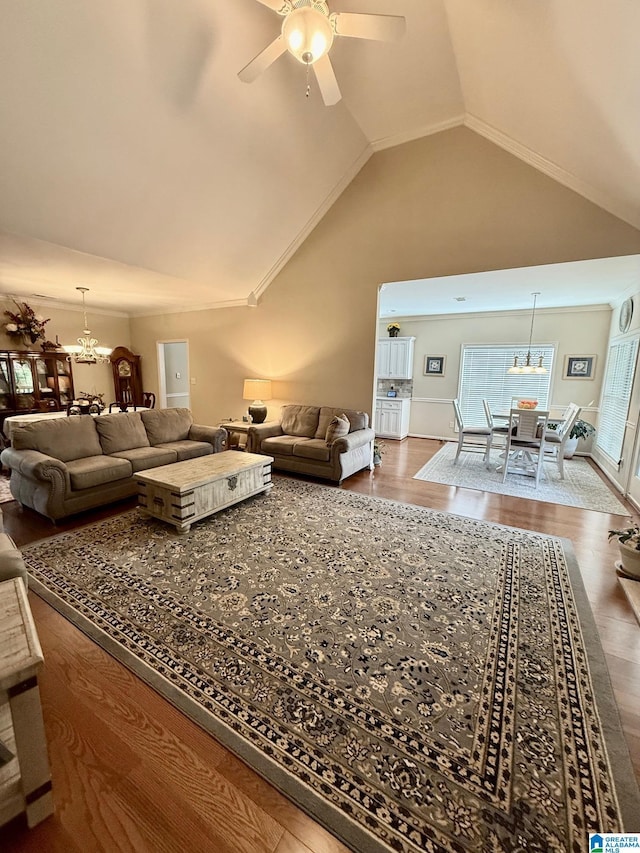living room with ceiling fan with notable chandelier, high vaulted ceiling, and wood finished floors