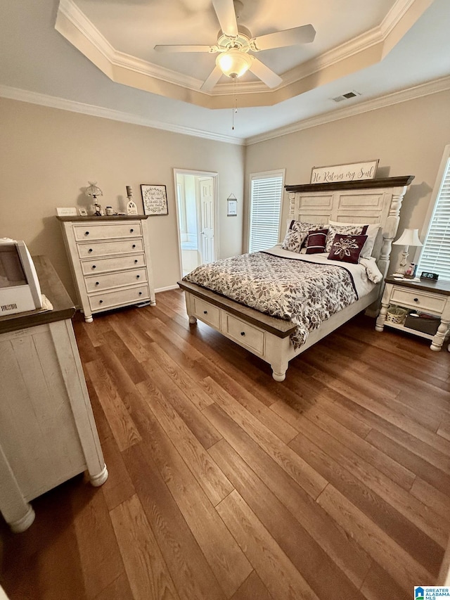 bedroom with dark wood finished floors, visible vents, crown molding, and a raised ceiling