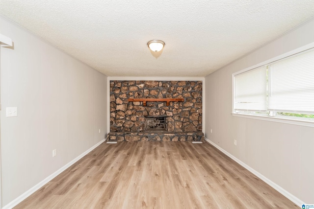 1625 Mann Dr, Birmingham, AL 35214 - unfurnished living room featuring a stone fireplace, baseboards, light wood-style flooring, and a textured ceiling
