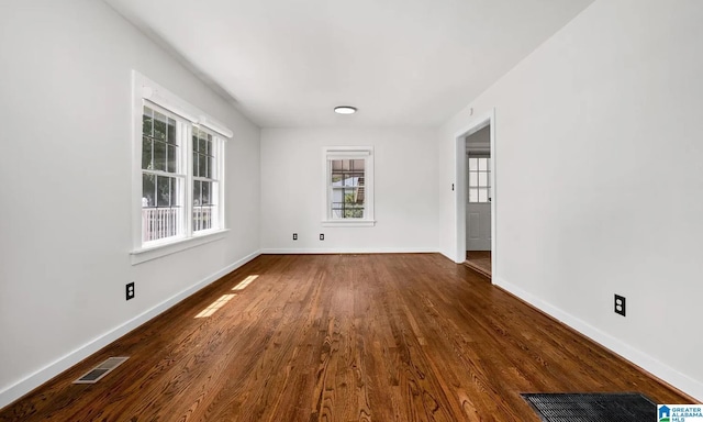 unfurnished room with baseboards, dark wood-style floors, and visible vents