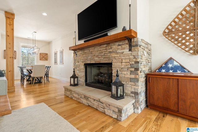 living area featuring baseboards, a stone fireplace, a chandelier, recessed lighting, and wood finished floors