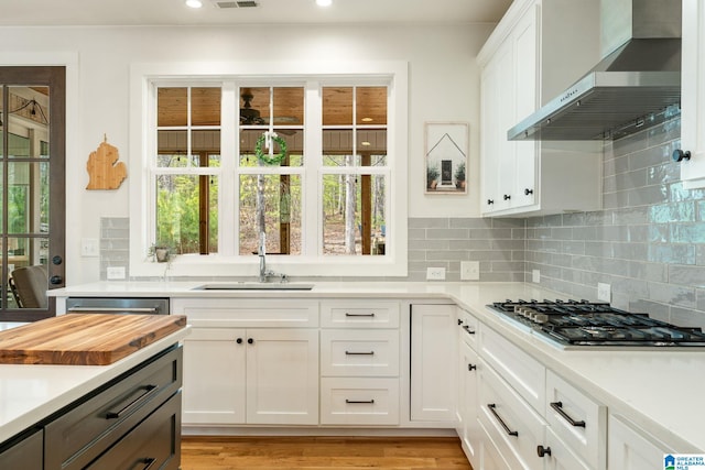 kitchen featuring wall chimney range hood, visible vents, light countertops, a sink, and backsplash