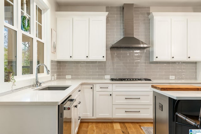 kitchen with wall chimney exhaust hood, dishwasher, a sink, light countertops, and gas cooktop