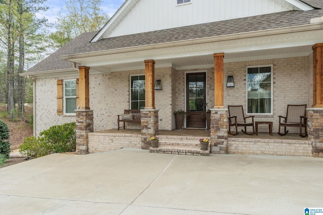 property entrance featuring board and batten siding, a shingled roof, covered porch, and brick siding
