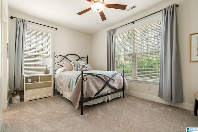 carpeted bedroom featuring visible vents, multiple windows, baseboards, and a ceiling fan