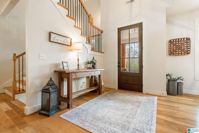 foyer entrance with visible vents, baseboards, stairway, and wood finished floors