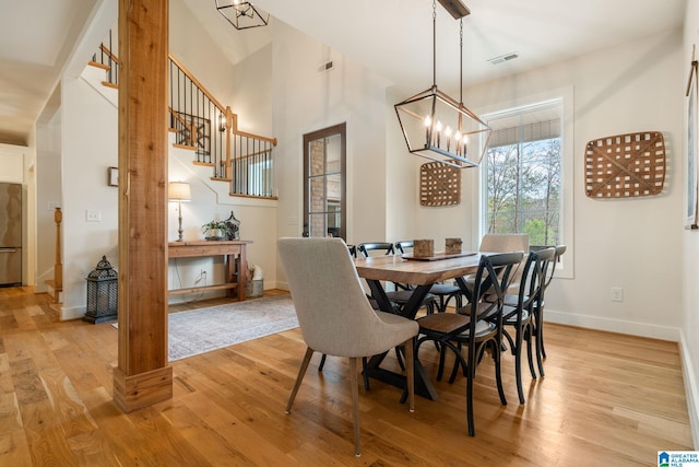 dining space featuring visible vents, baseboards, a chandelier, light wood finished floors, and stairway