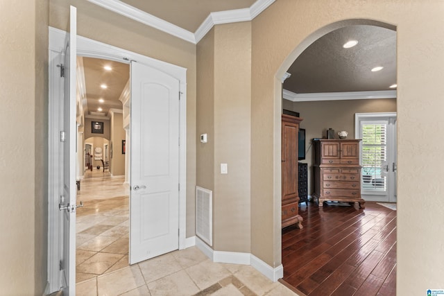 entrance foyer featuring arched walkways, ornamental molding, visible vents, a textured wall, and baseboards