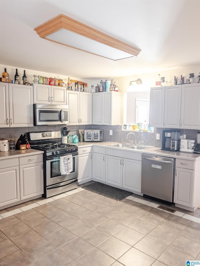 kitchen featuring tasteful backsplash, light countertops, white cabinetry, stainless steel appliances, and a sink
