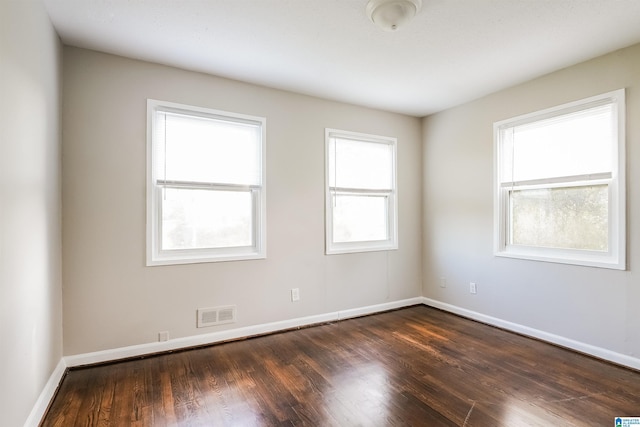 spare room with dark wood-style flooring, visible vents, and baseboards