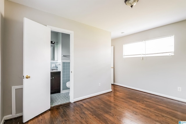 unfurnished bedroom with baseboards, dark wood finished floors, and ensuite bath