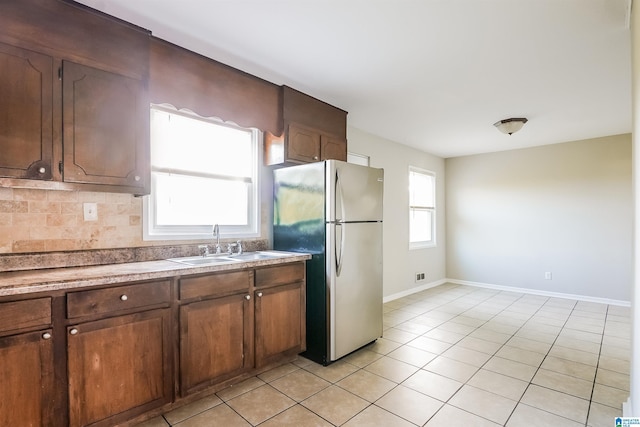 kitchen featuring light tile patterned floors, a sink, freestanding refrigerator, and decorative backsplash