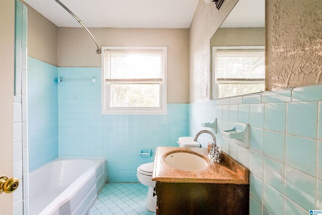 bathroom featuring washtub / shower combination, vanity, a wainscoted wall, toilet, and tile walls