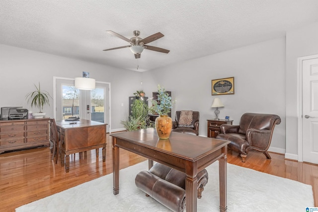 office space featuring baseboards, light wood finished floors, a textured ceiling, and a ceiling fan