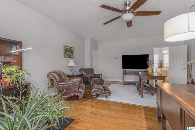 living room with light wood finished floors, a textured ceiling, ceiling fan, and baseboards
