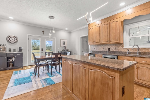 kitchen with tasteful backsplash, a sink, ornamental molding, and light wood-type flooring