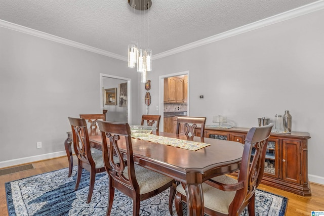 dining room featuring light wood-style flooring, ornamental molding, visible vents, a chandelier, and baseboards