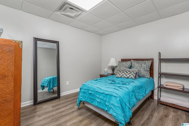 bedroom featuring visible vents, baseboards, a drop ceiling, and wood finished floors