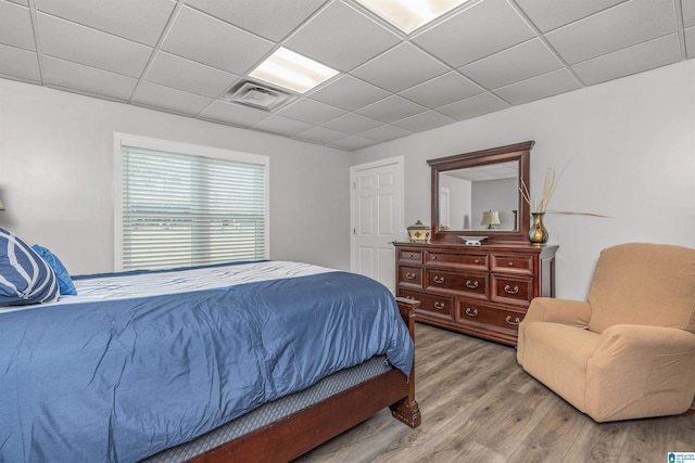 bedroom featuring light wood-style flooring, a paneled ceiling, and visible vents