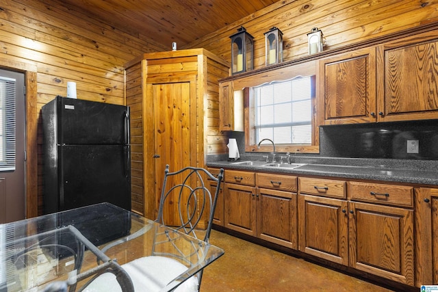 kitchen featuring a sink, freestanding refrigerator, dark countertops, wooden walls, and brown cabinetry