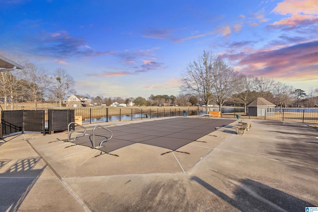 pool at dusk featuring a water view, fence, a fenced in pool, and a patio