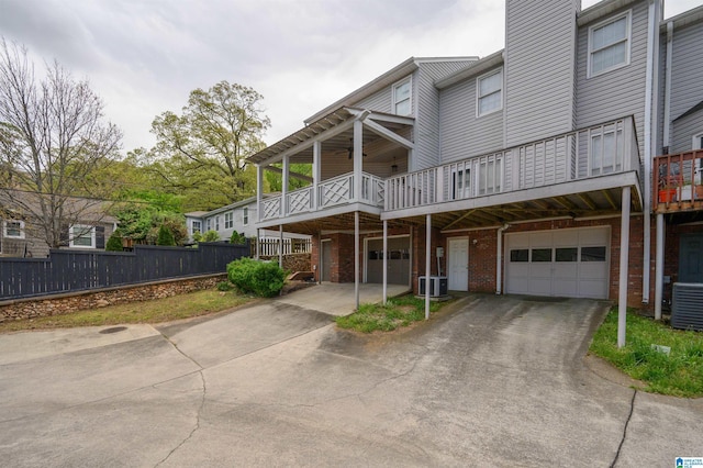 back of house with an attached garage, driveway, central AC unit, and brick siding