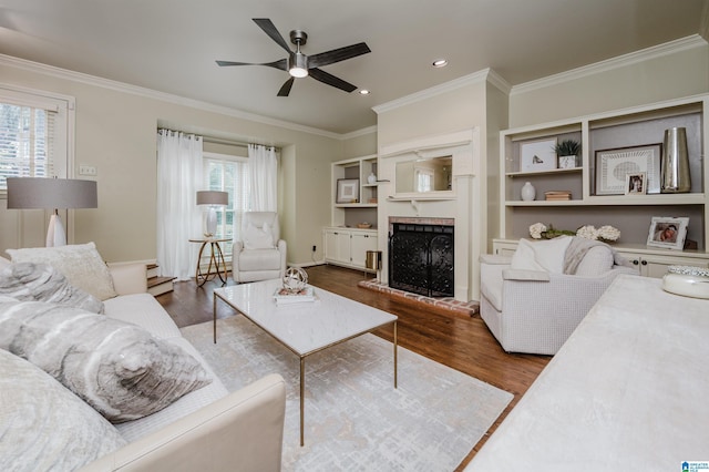living room featuring wood finished floors, ceiling fan, a fireplace, and ornamental molding
