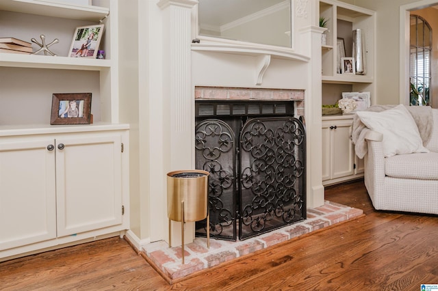 living room featuring built in shelves, a brick fireplace, ornamental molding, and wood finished floors