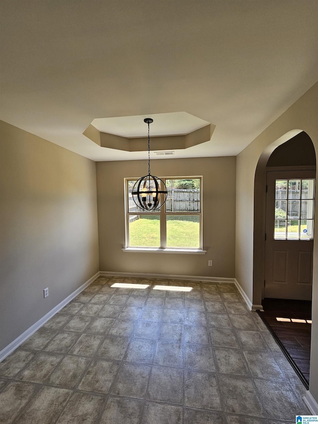 unfurnished dining area with a wealth of natural light, arched walkways, a tray ceiling, and baseboards