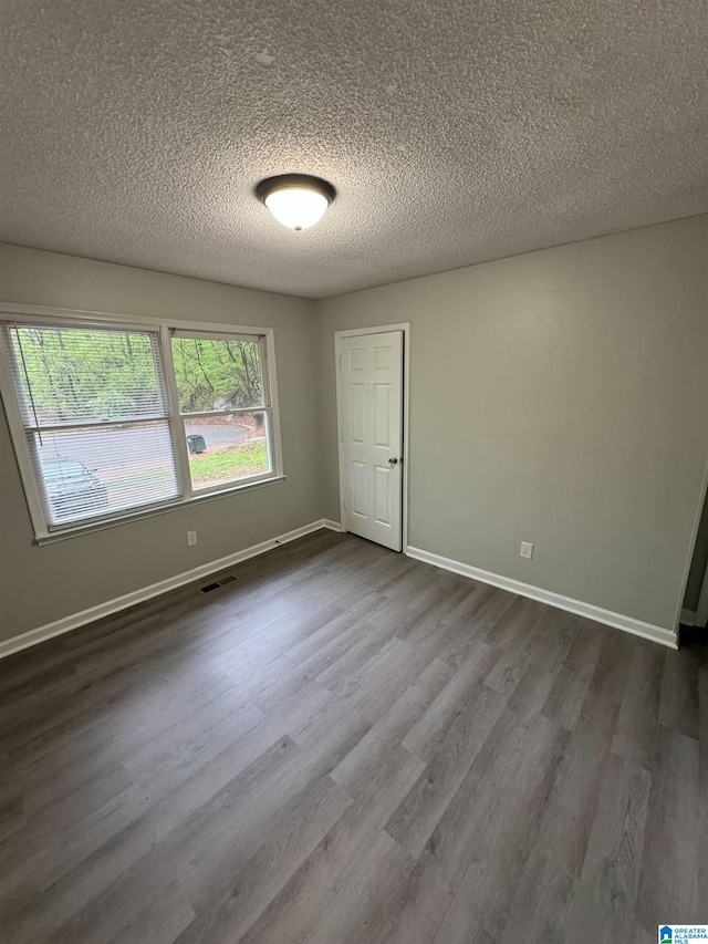 empty room featuring dark wood-type flooring, visible vents, baseboards, and a textured ceiling