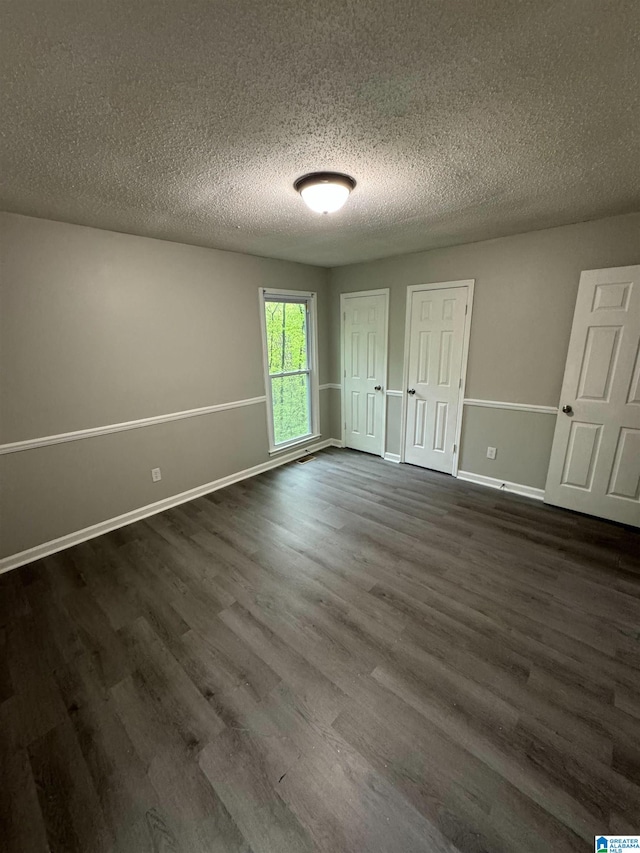 unfurnished bedroom featuring a textured ceiling, baseboards, two closets, and dark wood finished floors
