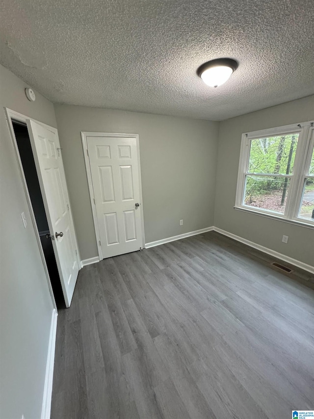 unfurnished bedroom with dark wood-style flooring, visible vents, baseboards, and a textured ceiling