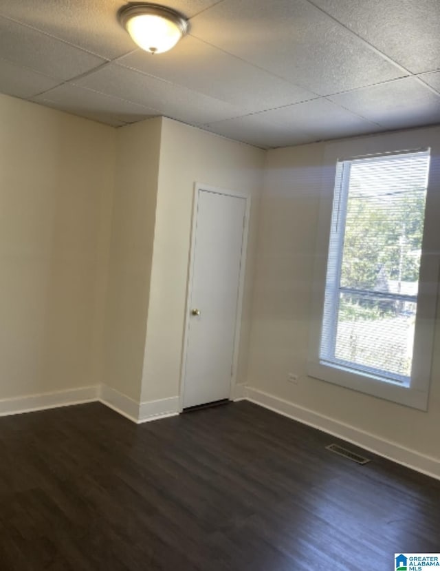 empty room featuring dark wood-type flooring, visible vents, baseboards, and a paneled ceiling