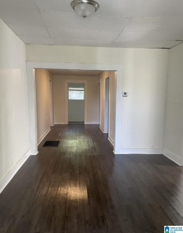 hall with dark wood-type flooring, visible vents, baseboards, and a paneled ceiling