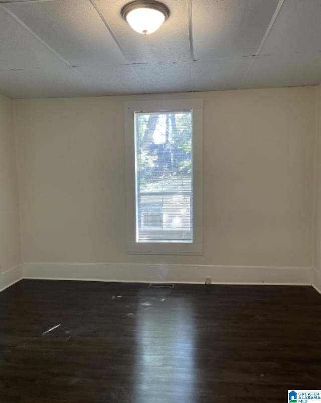empty room featuring a paneled ceiling, baseboards, and dark wood finished floors