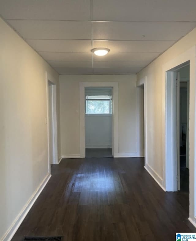corridor with dark wood-type flooring, a paneled ceiling, baseboards, and visible vents