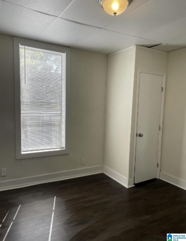 spare room featuring dark wood-type flooring, baseboards, and a paneled ceiling
