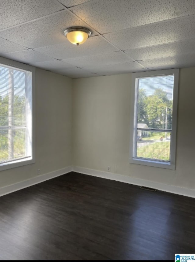 spare room with dark wood-type flooring, a paneled ceiling, baseboards, and visible vents
