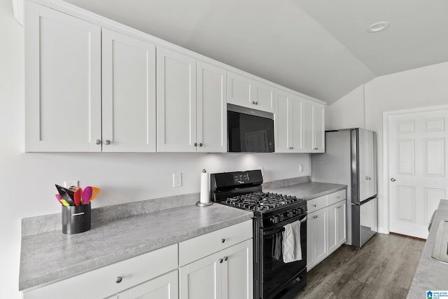kitchen featuring light countertops, vaulted ceiling, freestanding refrigerator, black gas range, and white cabinetry