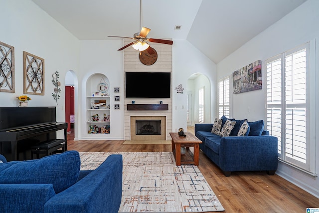 living room featuring arched walkways, built in features, a ceiling fan, and wood finished floors