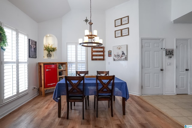 dining area with light wood-style flooring, high vaulted ceiling, and a notable chandelier