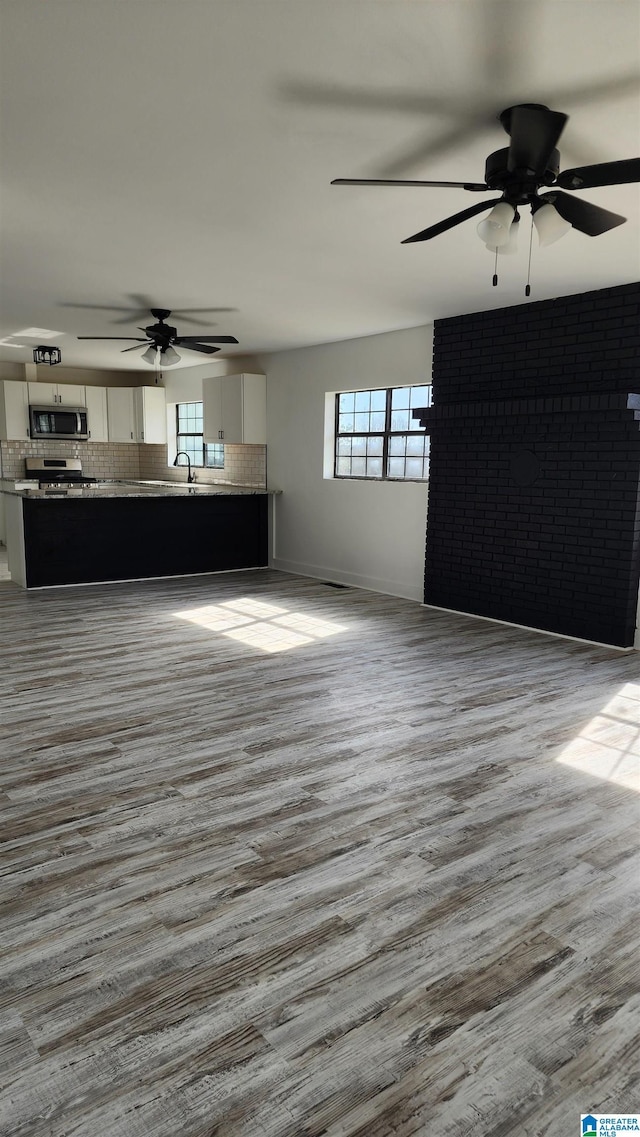 unfurnished living room with ceiling fan, baseboards, a sink, and wood finished floors